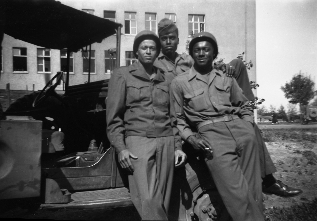 Gray-scale image of three people sitting on an old car